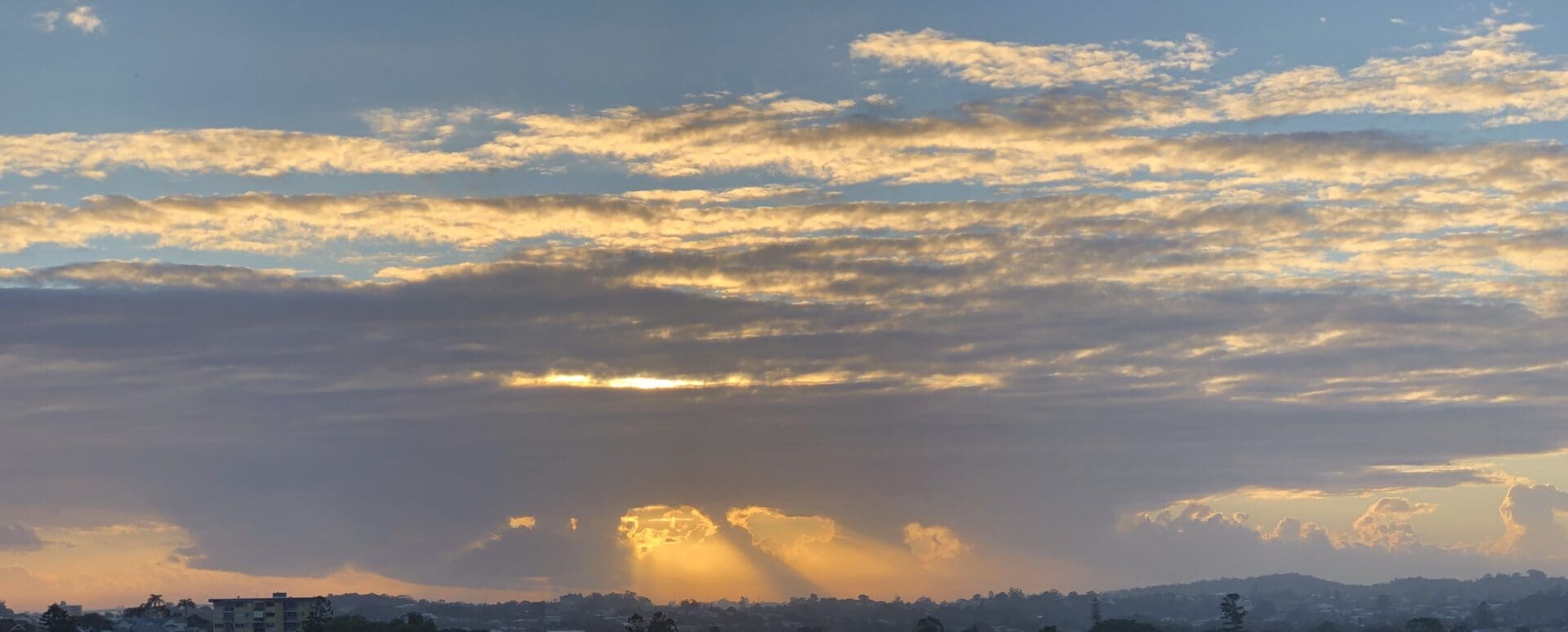 A cloudy sky with sun setting behind it.